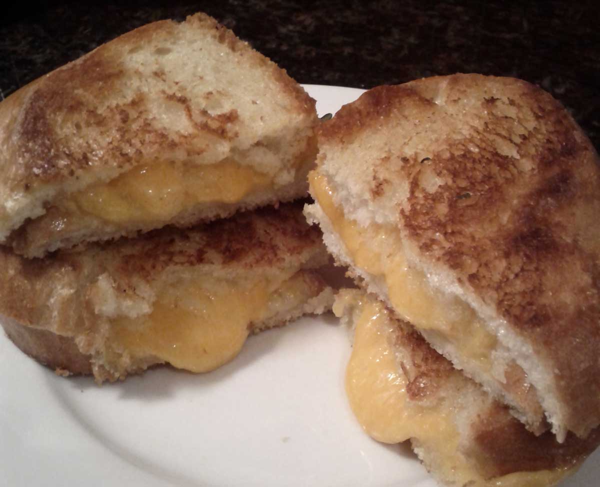 Two stacked grilled cheese sandwiches, cut in half, with cheese oozing out the centre.